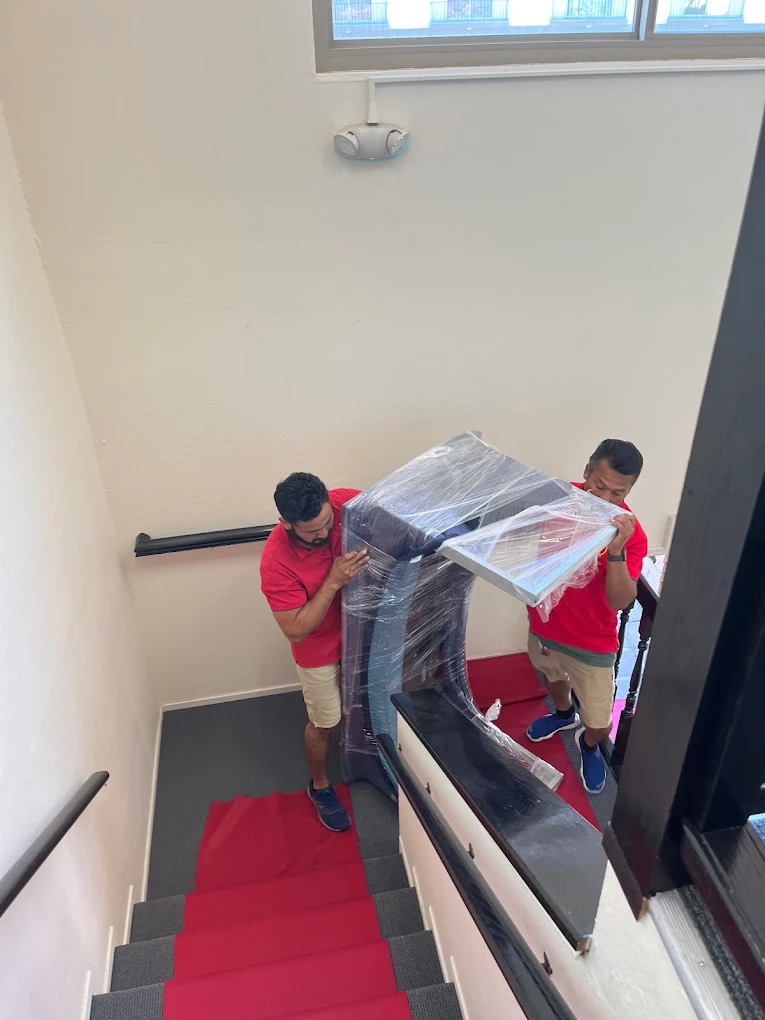 New Joy Moving movers wrapping a piano with protective plastic film
