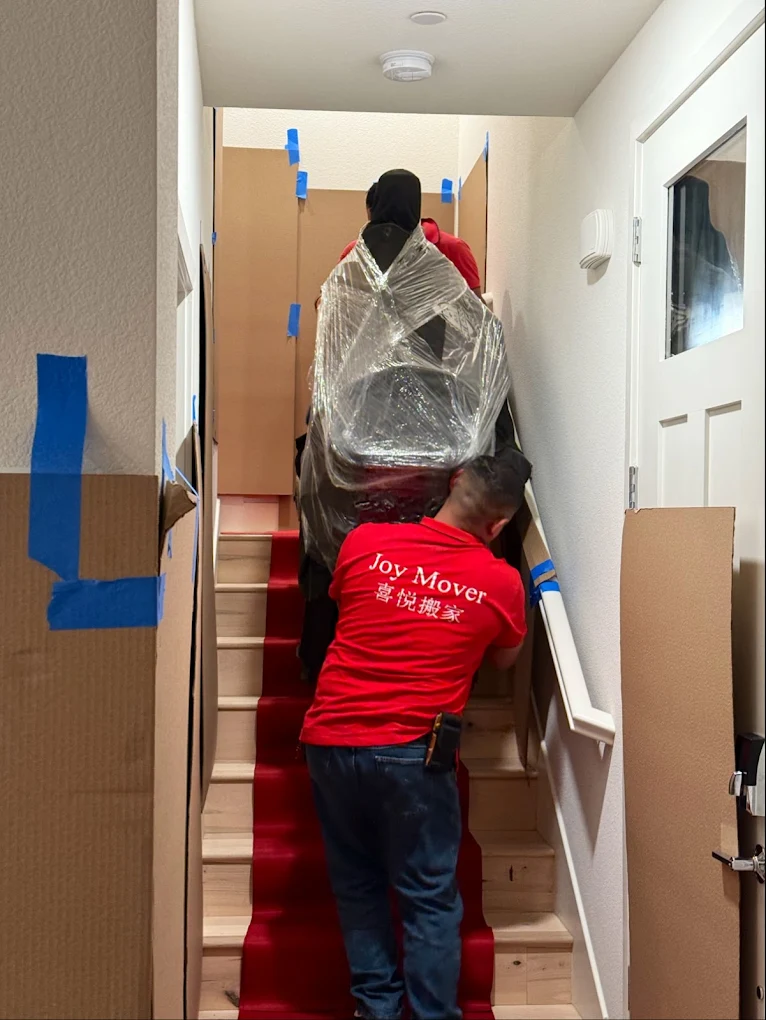 New Joy Moving movers carrying a wrapped item up a protected staircase