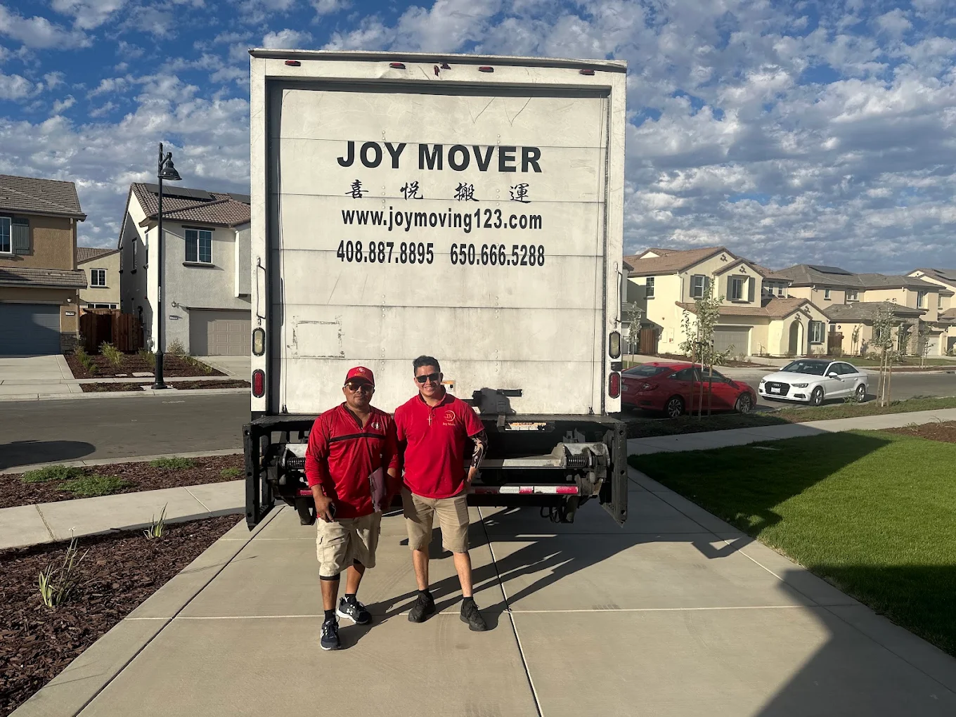 Two New Joy Moving movers standing in front of a residential moving truck